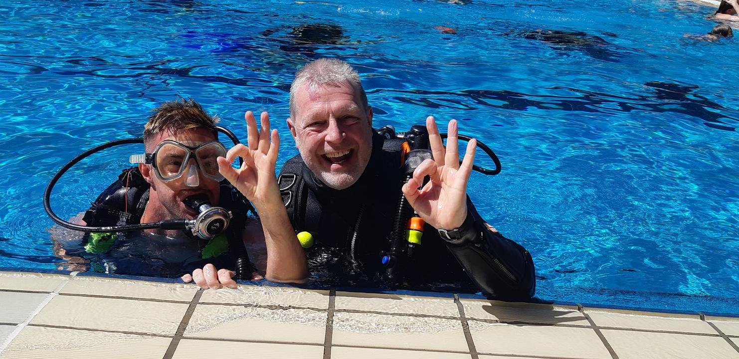 Zwei Taucher mit und ohne Beeinträchtigung lächeln und zeigen "OK"