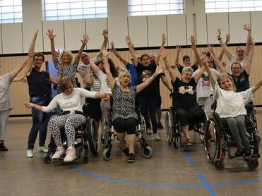 Foto von inklusiven Tanzangebot in Frechen. Alle Teilnehmenden freuen sich und halten die Hände hoch.