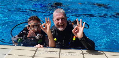 Zwei Taucher mit und ohne Beeinträchtigung lächeln und zeigen "OK"