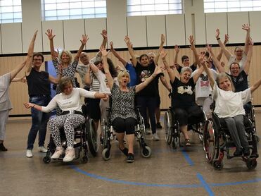 Foto von inklusiven Tanzangebot in Frechen. Alle Teilnehmenden freuen sich und halten die Hände hoch.